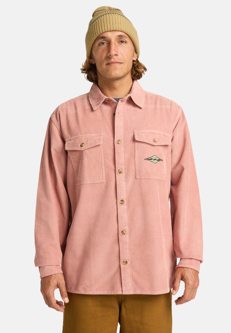 En ljusrosa kord skjorta med knäppning, två bröstfickor och en broderad logotypdetalj, samt en beige stickad mössa.