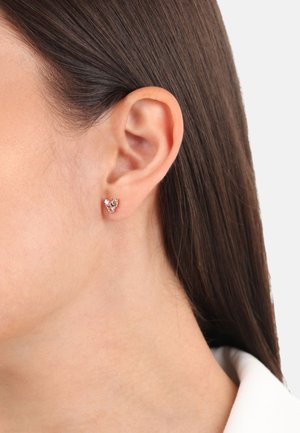 Orecchini a pendente in oro rosa a forma di cuore, con accenti di pietre preziose trasparenti e rosa, su uno sfondo semplice.