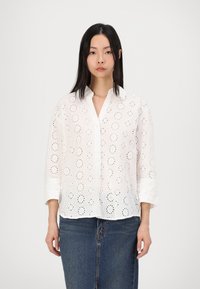 White cotton shirt with eyelet patterns, button-down front, and three-quarter sleeves. Paired with a denim skirt.