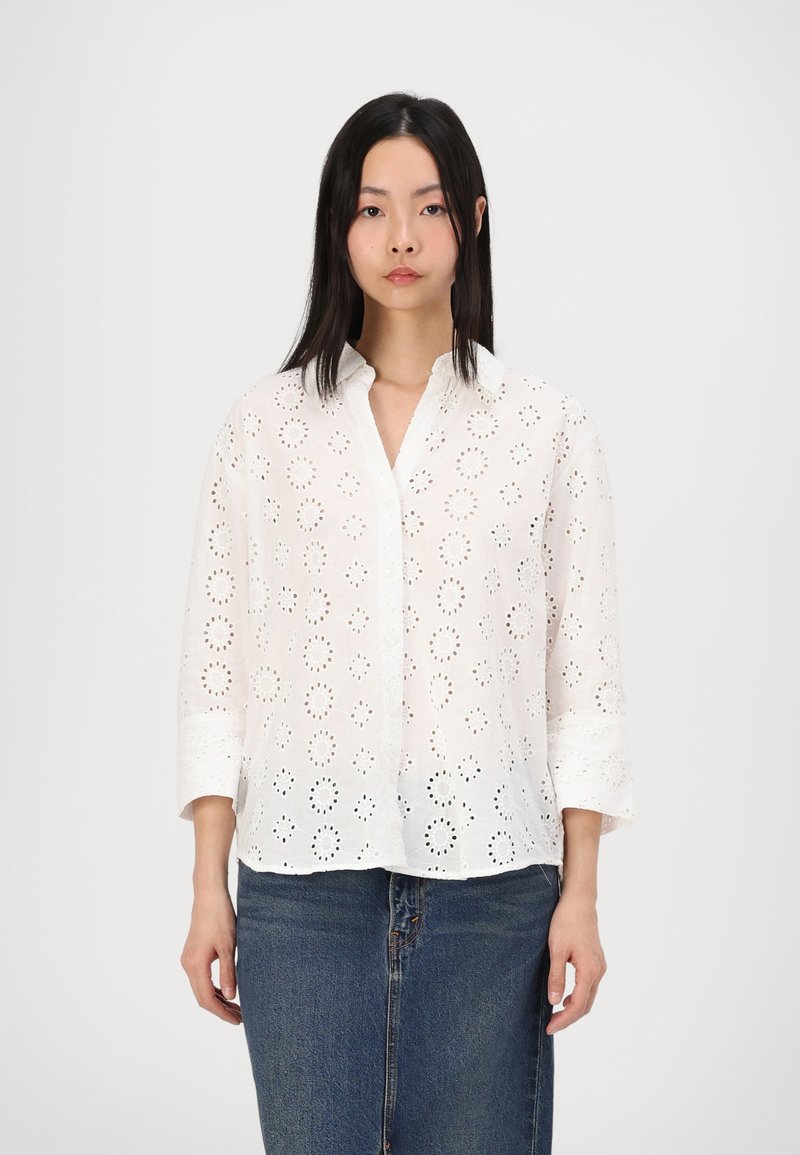 White cotton shirt with eyelet patterns, button-down front, and three-quarter sleeves. Paired with a denim skirt.