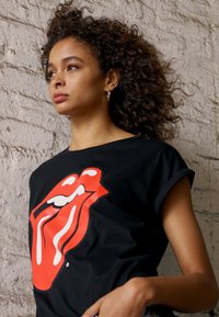 Sort T-shirt lavet af bomuld, med et stort rødt og hvidt Rolling Stones læber logo. Korte ærmer, løst fit, glat tekstur.