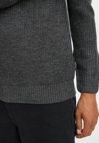 Dark gray ribbed sweater featuring a textured knit design and fitted cuffs, worn over black pants, highlighting its soft material.