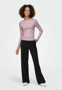 Jasnoróżowa bluzka z długim rękawem o prążkowanej strukturze i kwiatowym wzorze, zestawiona z czarnymi spodniami o szerokich nogawkach i białymi butami.
