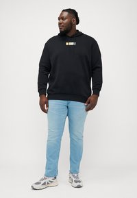 Sudadera negra con un gráfico en la parte frontal, jeans de mezclilla y zapatillas grises. La sudadera tiene un cordón y puños acanalados. Ajuste casual y relajado.