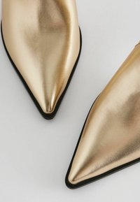 Kultaiset metalliset ballerinat kärjet osoittavat, joissa on sileä ja heijastava pinta sekä hienovarainen rakenne, varustettuna mustalla pohjalla ja tyylikkäällä muotoilulla.