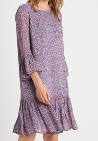 Robe à imprimé floral avec une base violette, des accents rouges et roses, des manches cloche trois-quarts, et un ourlet évasé à volants.