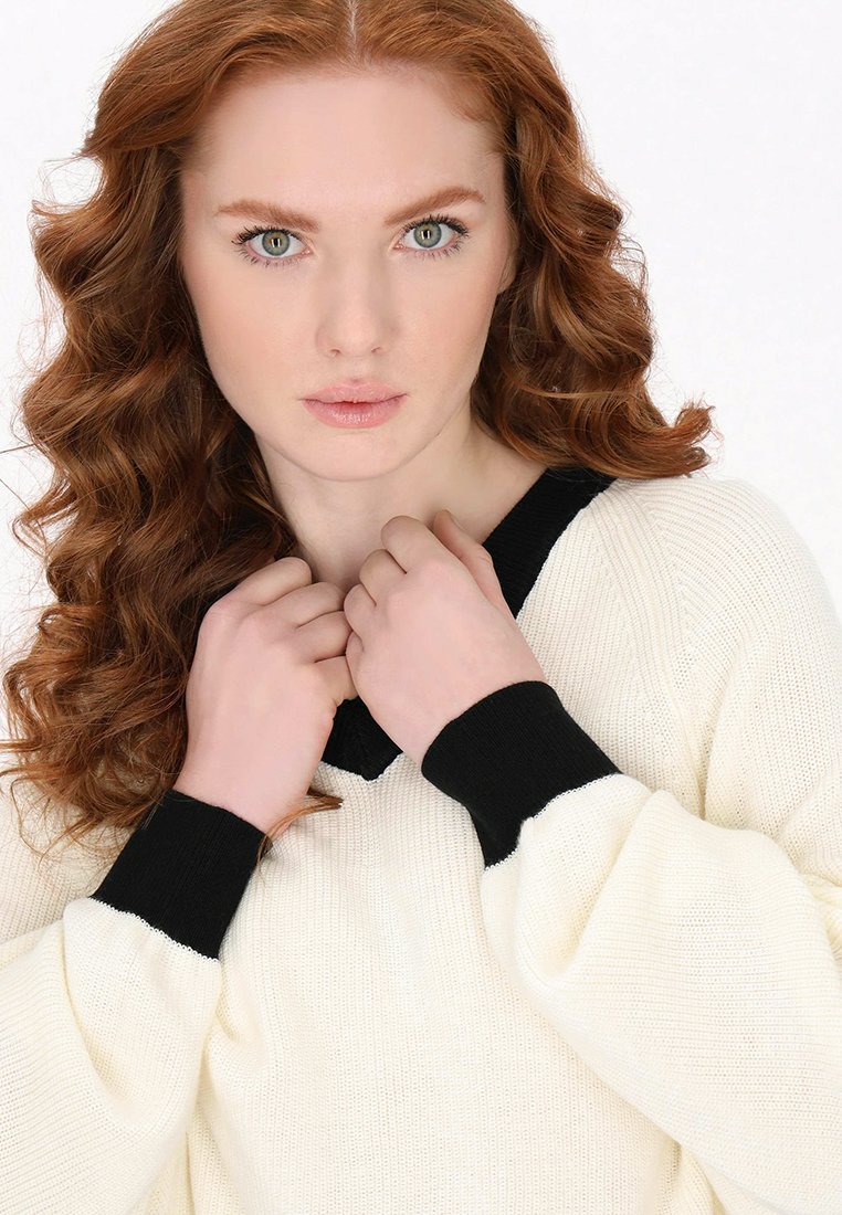 Übergroßer kremfarbener Pullover mit einem schwarzen V-Ausschnitt und Bündchen; strukturiertes Strickgewebe; lange Ärmel; weich und gemütlich im Aussehen.