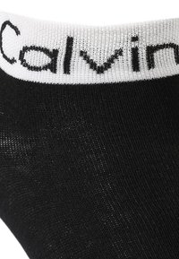 Sort ankelstrømpe med tekstureret stof og et hvidt elastikbånd med "Calvin Klein" i sort skrift.