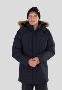 Parka bleu marine avec capuche en fourrure, fermeture �éclair à l'avant et plusieurs poches ; fabriqué en tissu isolant ; présente une finition extérieure texturée.