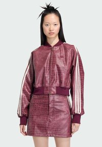 Burgundska bomber jakna s teksturom krokodila, s patentnim zatvaračem sprijeda, rebrastim rukavima i tri bijele pruge na svakom rukavu. Dodatna uska suknja.