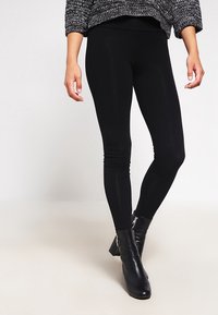 Svarta leggings gjorda av stretchigt material med en slät textur, med hög midja, tillsammans med svarta ankelboots med dragkedja.
