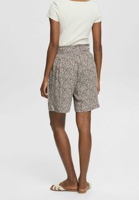 Hnědé šortky s vzorem a elastickým pasem, navržené v volném střihu. Spárovány se světlým přiléhavým topem a plochými sandály.