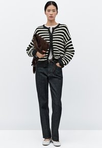 Pruhovaný pletený cardigan v černé a bílé barvě, uzavíratelný na knoflíky, v kombinaci s tmavými džínami a světlými šedými nazouvacími botami. Drží hnědou psaníčko.