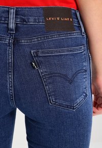 Jeans de mezclilla azul con corte slim, que cuentan con una etiqueta negra de Levi's en la cinturilla y un diseño distintivo en el bolsillo trasero.
