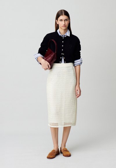 Cardigan noir avec boutons blancs, chemise rayée bleue et blanche, jupe midi blanche texturée et mocassins marron, portant un sac à main bordeaux.