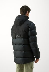 Geacă puffer neagră cu glugă, design matlasat și logo-ul proeminent "HH" pe spate. Textură netedă și margine scurtă.