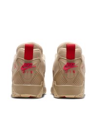 Beige Nike Air sneakers with red accents, padded collar, textured back panel, and rubber outsole with defined traction points.