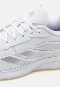 Białe sportowe buty z siateczkowymi wstawkami, gładkimi skórzanymi detalami i odblaskowymi akcentami. Posiadają teksturowane sznurowadła i wyściełany kołnierz.