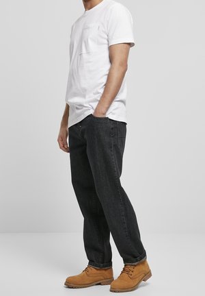 T-shirt en coton blanc avec une poche poitrine, associé à un jean en denim foncé et des bottes à lacets couleur beige, debout devant un fond neutre.