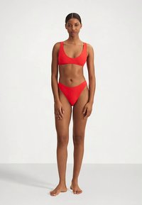 Conjunto de bikini rojo que incluye un sujetador tipo triángulo y braguitas de talle medio. Textura suave, costuras mínimas y diseño sencillo sin adornos.
