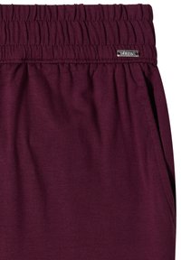Taille élastique sur un pantalon violet foncé avec une petite étiquette métallique rectangulaire de la marque fixée près du haut à droite.