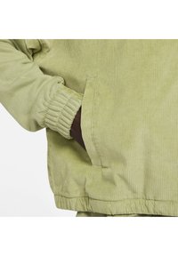 Lys grøn kordfløjl jakke med ribbet struktur, elastiske manchetter og sidelommer. Stoffet ser blødt og lidt shiny ud.