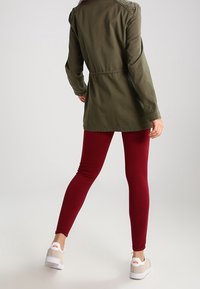 Olivgrön lättviktsjacka med spetsdetaljer på axlarna, tillsammans med bordeaux leggings och beige sneakers med vita sulor.