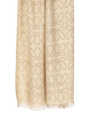 Beżowa tkana tkanina z kwiatowym wzorem w jaśniejszym beżu. Frędzlowy brzeg na dole dodaje tekstury. Miękki materiał o gładkim wykończeniu.