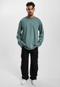 Long-sleeved teal shirt with crew neckline, paired with black cargo pants. White sneakers complete the outfit.