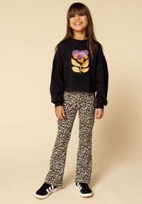 Zwarte cropped trui met een kleurrijk bloemenontwerp, gecombineerd met beige flared broek met luipaardprint en zwarte sneakers met witte strepen.