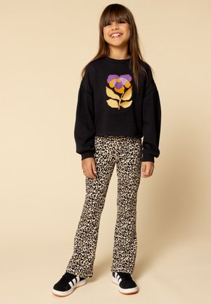Zwarte cropped trui met een kleurrijk bloemenontwerp, gecombineerd met beige flared broek met luipaardprint en zwarte sneakers met witte strepen.