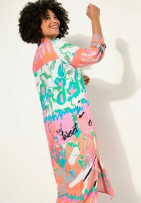 Robe à boutons multicolore avec des motifs floraux et abstraits en rose, vert et blanc. Manches longues avec poignets, fentes sur les côtés.