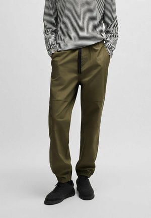Olijfgroene joggingbroek met een drawstring taille en elastische boorden, gemaakt van gladde stof. Draagt een zwart-wit gestreepte lange mouwen shirt.