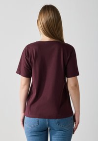 Burgunder farge crew-neck t-skjorte laget av myk stoff, med korte ermer og en avslappet passform, sammen med lyseblå denimjeans.