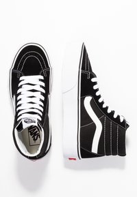 Un paio di sneakers alte Vans nere e bianche con lacci bianchi e la caratteristica striscia laterale, viste dall'alto e di lato.