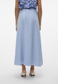 Ljusblå lång kjol i lätt tyg. Har ett elastiskt midjeband och slutar vid mitten av vaden, kombinerad med beiga högklackade sandaler.