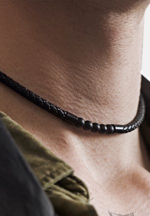 Svart flettet skinnkjede med sfæriske matte perler og metalliske detaljer, som ligger tett rundt halsen.