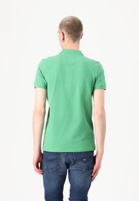 Grønn bomullspolo med korte ermer og klassisk krage, kombinert med mørkeblå jeans som har baklommer.