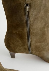 Maslinasto zeleni antilop gležnjači s niskom petom, sa bočnim zipom i glatkom teksturom. Naglašen s elegantnim dizajnom i minimalističkim stilom.