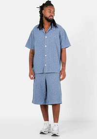 Blauwe korte mouwen herenoverhemd en bijpassende korte broek van gemusterde stof, met een relaxte fit, knopen en witte accenten.