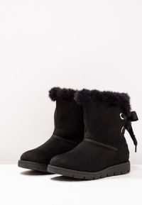Černé semišové kotníkové boty s umělou kožešinou na vršku, plochou gumovou podrážkou, bočním detailem v podobě stuhy a hladkým povrchem.