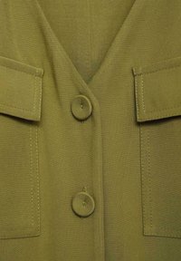 Olive green jacket featuring a V-neckline, two front pockets, and large buttons. Made of textured fabric with visible stitching details.