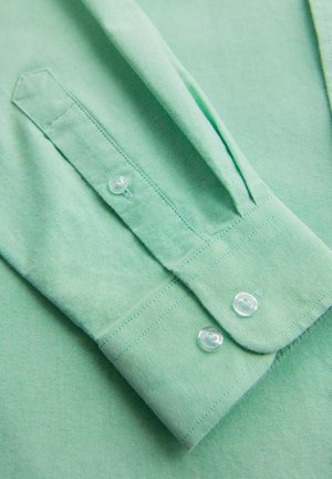 Camicia verde chiaro con bottoni, caratterizzata da una texture liscia, colletto a punta, piccoli bottoni e maniche piegate.