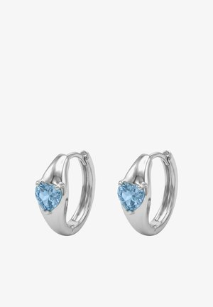 Silberne Creolen, jeweils mit einem herzförmigen blauen Edelstein vorne besetzt, gestaltet mit einer glatten und polierten Oberfläche.