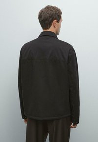 Black, long-sleeve jacket with a straight cut, buttoned cuffs, and a pointed collar. Smooth texture and minimalistic design.