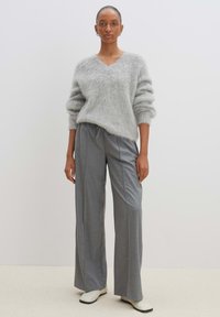 Helle graue, flauschige Sweater mit V-Ausschnitt und Ballonärmeln; kombiniert mit lockeren, hellgrauen, hoch taillierten Hosen; glatte, weite Beine.