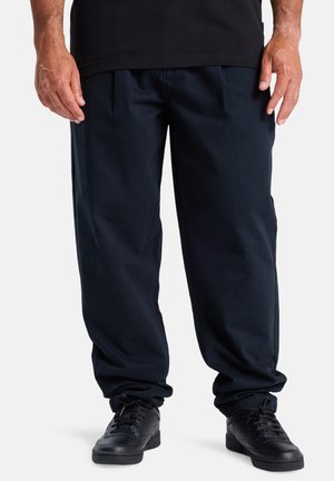 Dark navy pants with a relaxed fit, made from soft fabric, featuring pleats and tapered cuffs. Paired with black sneakers.