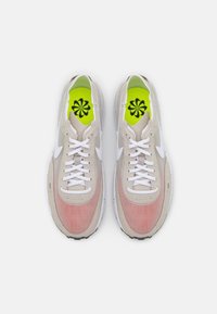 Baskets de sport beiges et roses avec un design en maille, un marquage blanc et des semelles intérieures vert vif à motif floral.