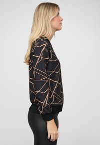 Schwarzes Sweatshirt mit geometrischem rosegoldenem Muster, langen Ärmeln, gerippten Bündchen und Saum. Glatte Textur, lockere Passform und seitliche Nahtdetails.