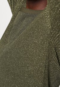 Olijfgroen geribbeld top met een textuurbreiwerk van metallic draden en een ronde halslijn. Zichtbare stiksels langs de randen.